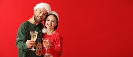 Young couple in stylish Christmas clothes and with glasses of champagne on color background with space for text