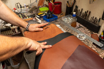 Close up of an latin old man hands working leather. Saddler making a leather handbag craftsman.