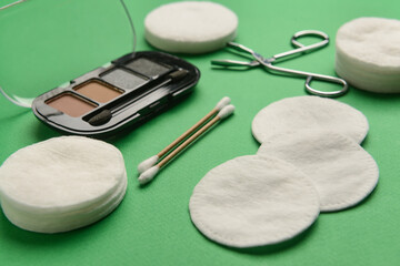 Obraz na płótnie Canvas Clean cotton pads, cotton buds and eyeshadows on green table, closeup