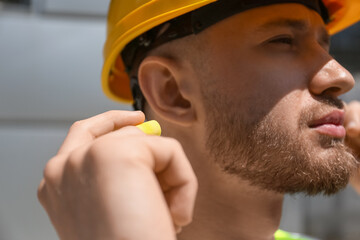 Male worker putting ear plug outdoors, closeup - obrazy, fototapety, plakaty