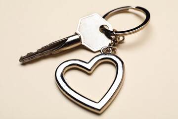 Key with heart shaped keychain on beige background, closeup