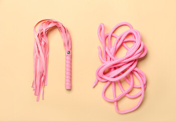 Whip and rope from sex shop on color background