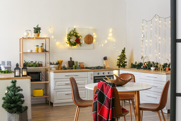 Interior of light modern kitchen with Christmas trees, decor and glowing garland