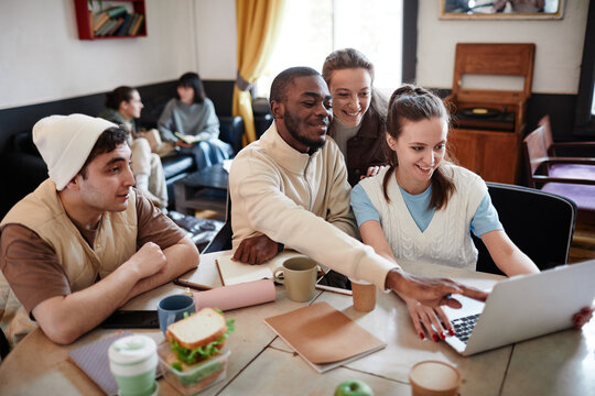 Group of college students sitting at the table and studying together using laptop