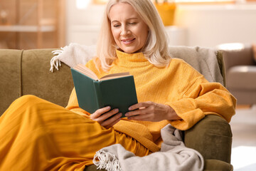 Beautiful mature woman reading book at home on autumn day