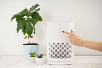 Woman turning on modern air purifier in the room.
