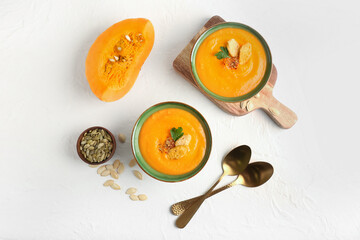 Bowls with delicious pumpkin cream soup and seeds on light background