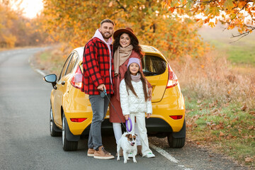 Parents with little daughter and cute dog near yellow car on autumn day