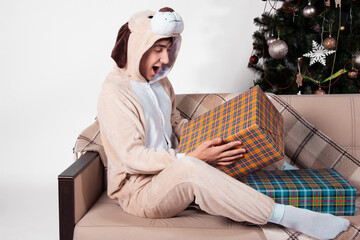 A joyful guy in pajamas sits on the couch with New Year's gifts. White background.