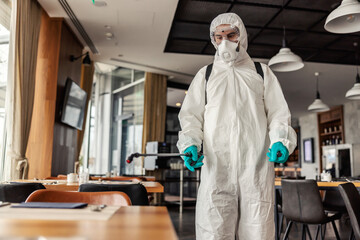 A determined to win COVID19. Man fights against the coronavirus in a temporarily isolated restaurant. With a worried expression on his face and in protective clothing, he disinfects table