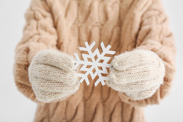 Fototapeta na wymiar Woman in warm gloves holding snowflake on light background, closeup