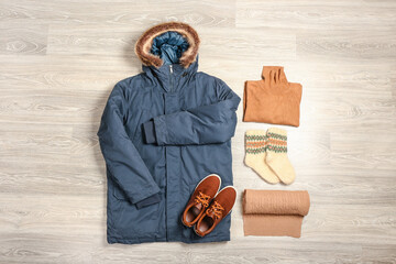 Winter jacket, sweater, socks, scarf and shoes on light wooden background © Pixel-Shot