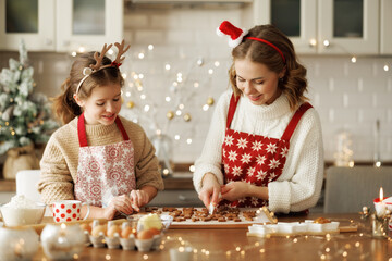 Happy family mother and girl daughter decorating Christmas gingerbread cookies after baking