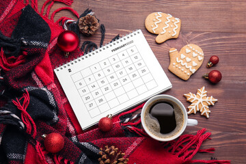 Fototapeta na wymiar Paper calendar for February 2022, cup of coffee, plaid and Christmas decor on wooden background