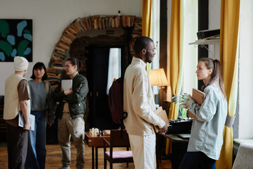 Group of students with books talking to each other while standing in the library after lessons