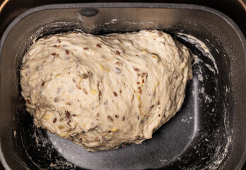 Close-up view of kneading wheat dough with seeds in a metal container of a bread maker. Homemade bread.