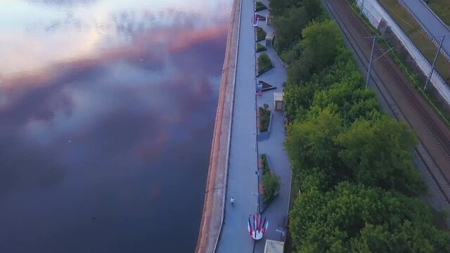 Clean lake next to the park road. Clip. The road along the green trees next to the crystal clear lake in which the sunset is reflected.