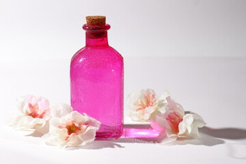 Fototapeta na wymiar Pink glass bottle with flowers, cosmetic container with reflection