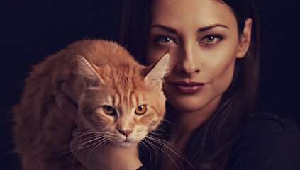 Beautiful make-up woman holding and hugging with love her red maine coon kitten. Closeup portrait. Art on black background
