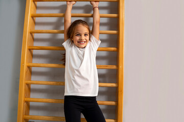Cute, adorable little girl hanging from wooden gym ladders and smiling, kids physical health. 