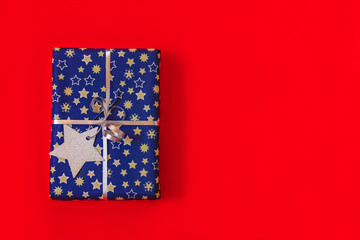 close up festive gift box blue and silver colors with paper christmas star decoration on red background with copy space