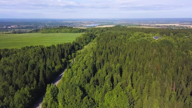 Wonderful landscape view from a bird's-eye view. Clip. A summer green forest with a road for cars next to the field and in the background a small provincial town with fields and small houses