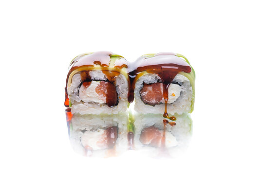 Two pieces of Japanese sushi roll with avocado slices on top served with unagi sauce. Salmon, cream cheese inside roll. inside out roll isolated on white background. Copy space image with  reflection
