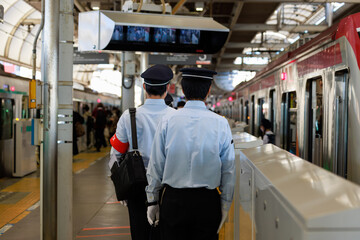 駅のプラットフォームで乗車前確認をする赤い腕章をした見習い車掌