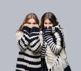 Two  girl wearing knit hat, scarf, sweater and gloves posing against   blue  background.