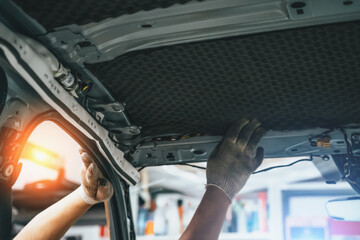 Worker hands glues soundproofing material to inside of car roof. Process of car sound insulation installation.