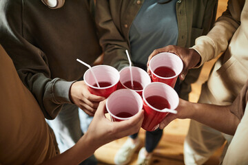 Close-up of young people toasting with plastic cups with alcohol drinks at a party