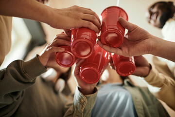 Low angle view of group of teenagers toasting with plastic cups and drinking cocktails at a party