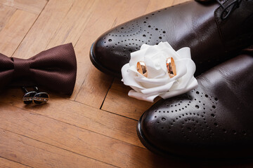 Men's accessories, boutonniere, gold rings, bow tie leather shoes of the groom on a wooden background. Businessman clothing detail concept. Luxury men's accessories. Stylish men's shoes, wedding