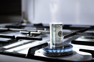 Concept of gas crisis. 100 dollar bank note is burning on kitchen stove. Cash money. High prices of...