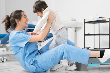 Physiotherapist hugging a little boy with a disability at rehabilitation clinic. Kid with cerebral...