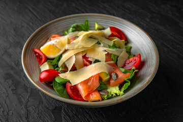 Nutritious, healthy, dietary salmon, avocado, pumpkin seed and greens salad in a ceramic plate on a dark textured background. Restaurant menu Isolated on black