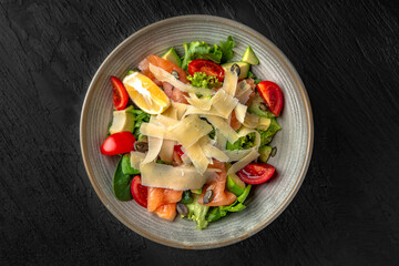Nutritious, healthy, dietary salmon, avocado, pumpkin seed and greens salad in a ceramic plate on a dark textured background. Restaurant menu Isolated on black