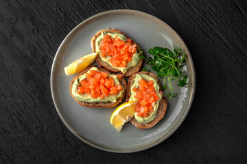 Bruschetta with salmon on guacamole in a ceramic plate on a dark textured background. Restaurant menu Isolated on black
