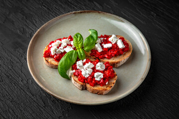 Bruschetta with baked pepper and cheese in a ceramic plate on a dark textured background. Restaurant menu Isolated on black