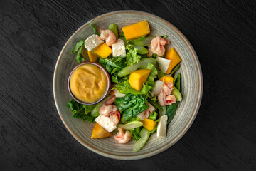 Avocado, shrimp, mango and greens salad with sauce in a ceramic plate on a dark textured background. Restaurant menu Isolated on black