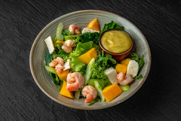 Avocado, shrimp, mango and greens salad with sauce in a ceramic plate on a dark textured background. Restaurant menu Isolated on black