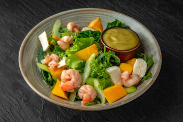Avocado, shrimp, mango and greens salad with sauce in a ceramic plate on a dark textured background. Restaurant menu Isolated on black