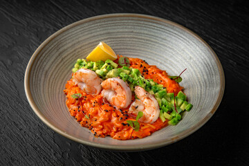 Delicate risotto with shrimps and avocado in a ceramic plate on a dark textured background. Restaurant menu Isolated on black