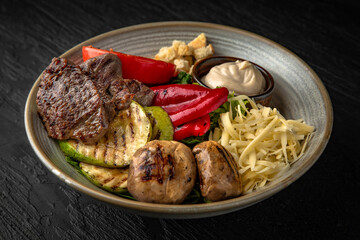 Grilled beef medallions with vegetables and mushrooms in a ceramic plate on a dark textured background. Restaurant menu Isolated on black