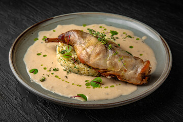 Rabbit leg baked with rice in sauce in a ceramic plate on a dark textured background. Restaurant menu Isolated on black