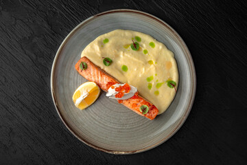 Salmon fillet with mascarpone, red caviar and tender puree in a ceramic plate on a dark textured...