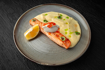Salmon fillet with mascarpone, red caviar and tender puree in a ceramic plate on a dark textured background. Restaurant menu Isolated on black