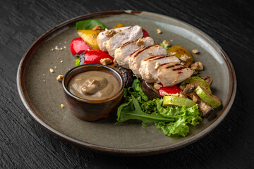 Grilled chicken steak with vegetables and sauce in a ceramic plate on a dark textured background. Restaurant menu Isolated on black