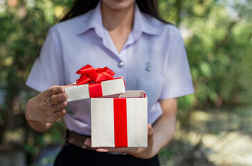 Female student opens a gift box with a red bow in her hand. Selective focus