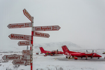 Route direction pole with different cities and North Pole with red planes in the background,...